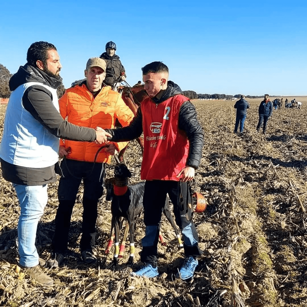 Imagen de José Galán (soltador) con galgo en un campo y dos hombres al frente dándose la mano